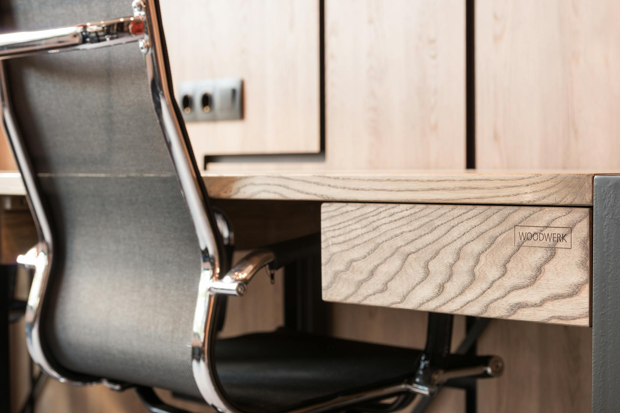 A contemporary office setup featuring a wooden desk and sleek metal chair with a minimalist design.
