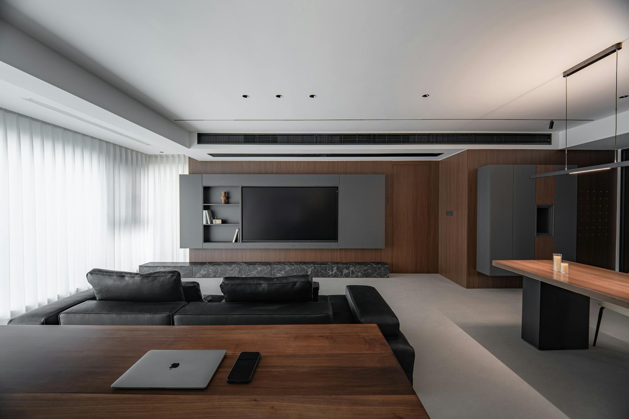 Spacious modern living room with minimalist design, featuring black couches and a wooden desk.
